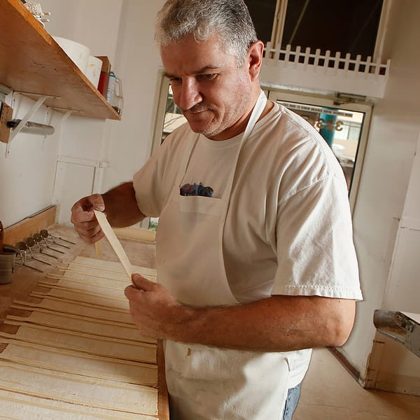 Nicolas Paré in a white apron hand-shaping strips of dough at a flour-dusted workbench in the bakery