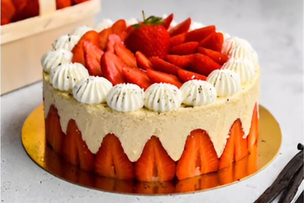 Strawberry Fraisier cake with halved strawberries around the sides and piped cream rosettes on top
