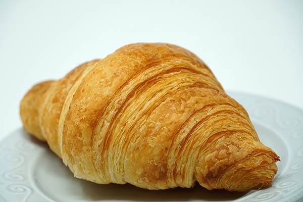 Golden butter croissant with crisp flaky layers on a white plate
