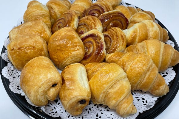 Party platter piled with mini croissants, pains au chocolat, and swirled fruit danishes on a lace doily