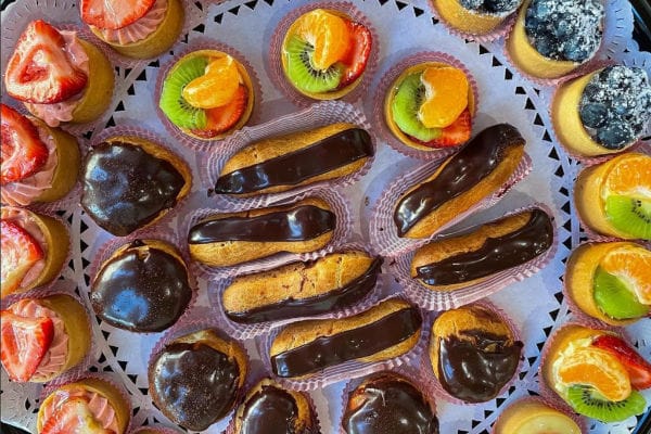 Platter of mini chocolate eclairs and fruit tartlets topped with kiwi, orange, strawberries, and blueberries