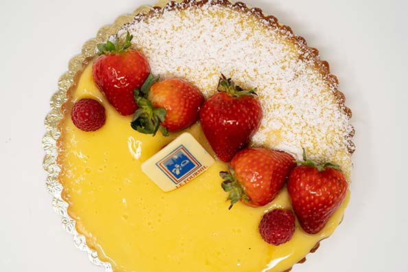 Whole passion fruit tart topped with fresh strawberries, raspberries, and powdered sugar